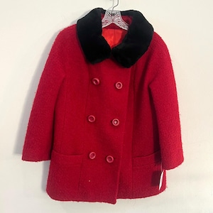 May include: A red double-breasted coat with a black faux fur collar hangs on a hanger. The coat has two rows of buttons and two front pockets. The coat is hanging against a white wall.