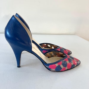 May include: A pair of blue and pink high-heeled shoes with a cut-out design. The shoes are made of leather and have a pointed toe.