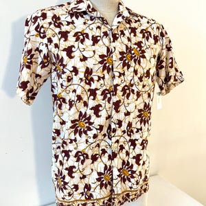 Peut inclure: Une chemise à manches courtes boutonnée, avec un fond blanc et un motif floral répété dans des tons marron et jaune. La chemise est présentée sur un mannequin et présente un col et un ourlet droit.