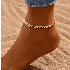 May include: A gold anklet with a delicate chain and small round beads. The anklet is worn on a person's ankle.