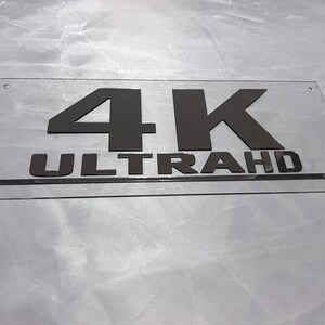 May include: A clear acrylic sign with black lettering that reads "4K ULTRA HD".