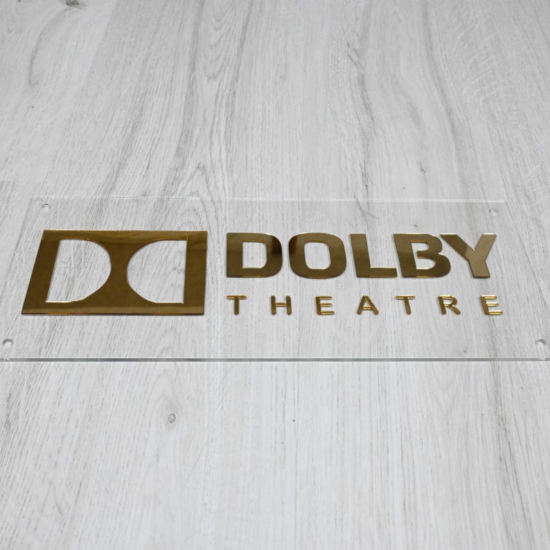 May include: A gold-colored sign with the text "DOLBY THEATRE" on a clear acrylic background.