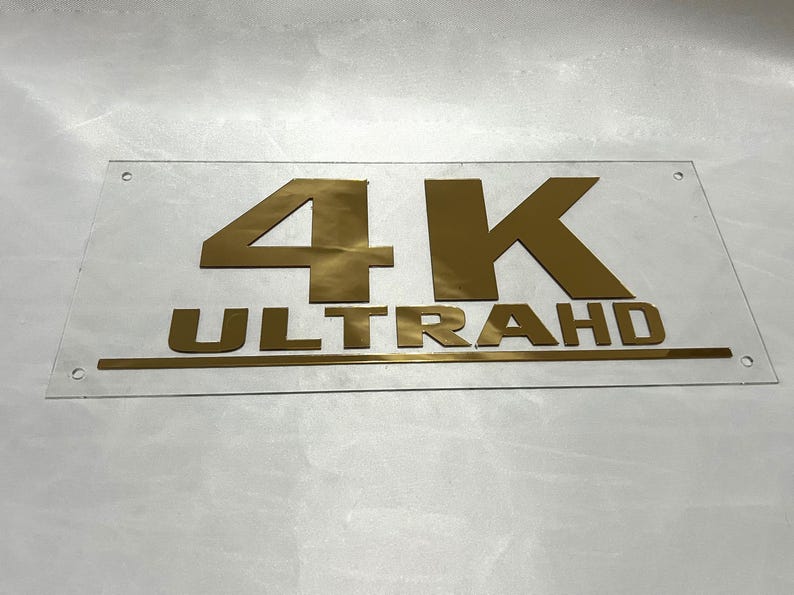 May include: A clear acrylic sign with gold lettering that reads "4K ULTRA HD".