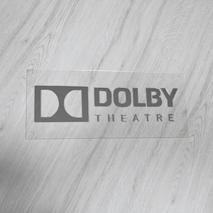 May include: A clear acrylic sign with a silver Dolby Theatre logo. The logo features the Dolby logo and the words "Dolby Theatre".