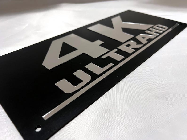 May include: Black rectangular sign with silver lettering that reads "4K ULTRA HD".