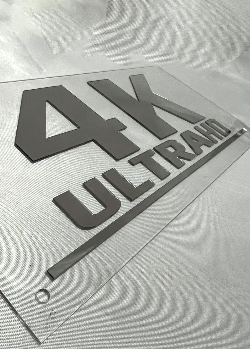 May include: A clear acrylic sign with the text "4K ULTRA HD" in black raised lettering.