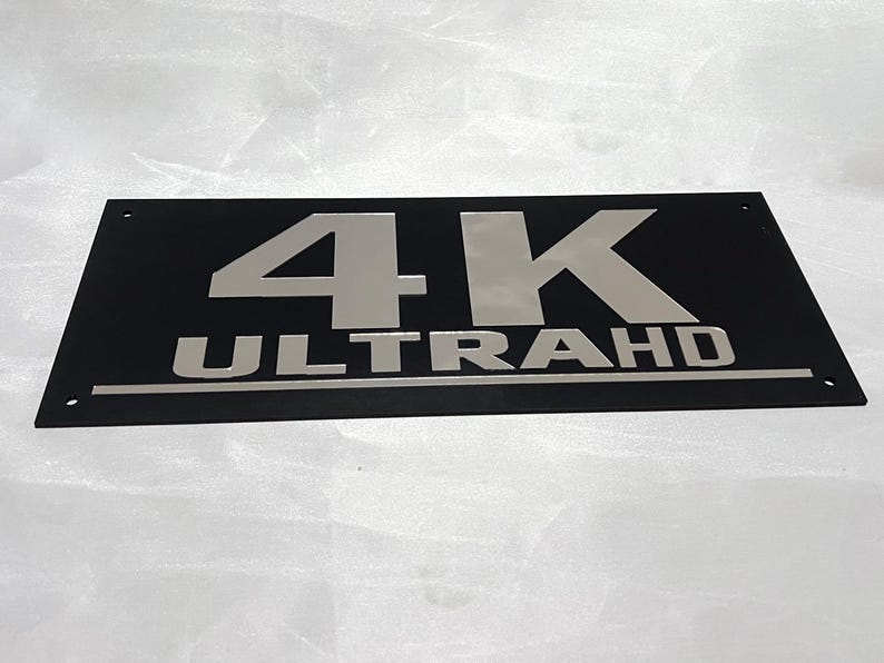 May include: A black rectangular sign with silver lettering that reads "4K ULTRA HD".