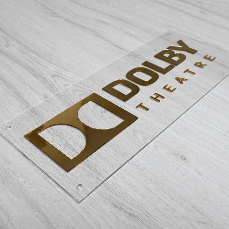 May include: A clear acrylic sign with gold lettering that reads "Dolby Theatre".