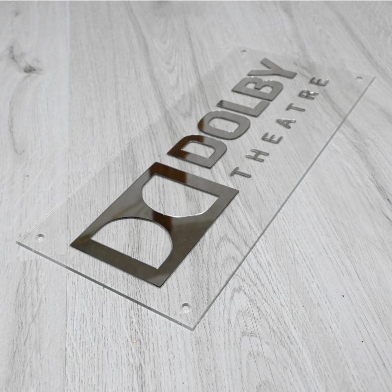 May include: A clear acrylic sign with a silver metallic finish. The sign reads "Dolby Theatre".