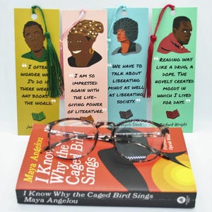 May include: Four bookmarks with colorful backgrounds and illustrations of people. Each bookmark features a quote about reading. The quotes are by James Baldwin, Toni Morrison, Angela Davis, and Richard Wright. The bookmarks are on top of a copy of the book "I Know Why the Caged Bird Sings" by Maya Angelou.