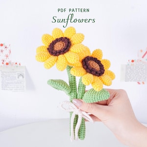 May include: A handmade crochet bouquet of sunflowers. The flowers have bright yellow petals, brown centers, and green stems and leaves. The bouquet is tied with a white ribbon. The text "PDF PATTERN Sunflowers" is at the top.