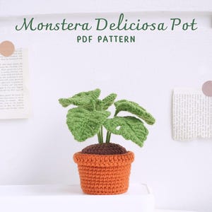 May include: A crocheted Monstera Deliciosa plant in a terracotta pot. The plant has green leaves with holes and the pot is orange. The image includes the text "Monstera Deliciosa Pot PDF PATTERN".