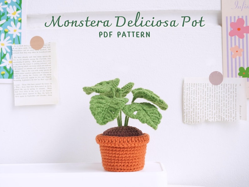 May include: A crocheted Monstera Deliciosa plant in a terracotta pot. The plant has green leaves with holes and the pot is orange. The image includes the text "Monstera Deliciosa Pot PDF PATTERN".