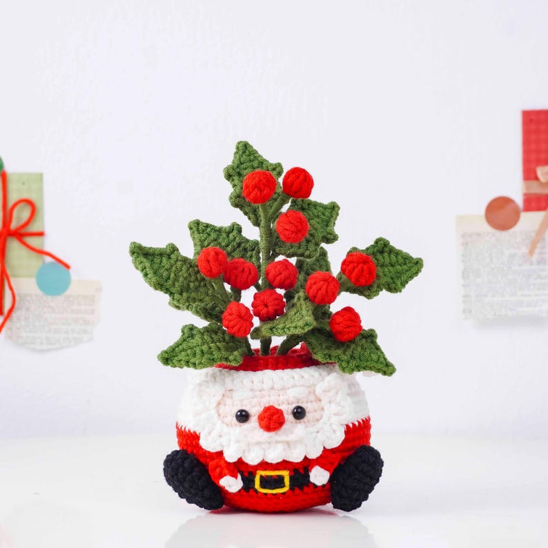 May include: A handmade crochet Santa Claus planter, featuring a red and white outfit with a black belt and boots. The planter holds a green crochet plant with red berries, creating a festive holiday decoration.