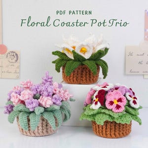 May include: Three crocheted floral pot designs. The pots are brown with green leaves and colourful flowers in shades of pink, purple, and white. The text "PDF PATTERN Floral Coaster Pot Trio" is at the top.