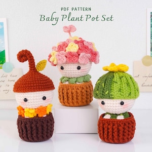 May include: Three crocheted figures in brown pots labeled Baby Plant Pot Set. The left figure has a brown acorn-like top, the center has a pink and yellow floral top, and the right has a green cactus top with a yellow flower. All have pale faces.