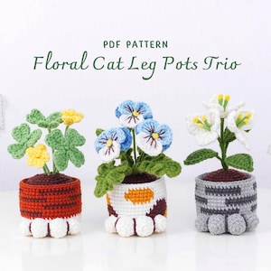May include: A trio of crochet flower pots, each designed to resemble cat paws. The pots are filled with crocheted flowers in yellow, blue, and white. The text "PDF PATTERN Floral Cat Leg Pots Trio" is displayed at the top.