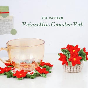May include: A clear glass teacup sits on a crocheted poinsettia coaster. A small crocheted pot filled with red poinsettia flowers is next to the cup. The words "PDF PATTERN Poinsettia Coaster Pot" are at the top.