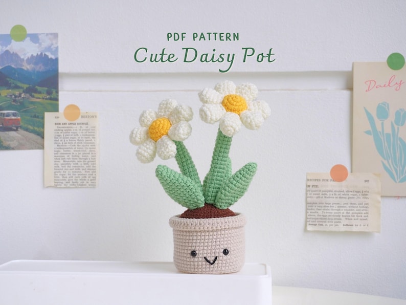 Puede incluir: Un patr&oacute;n de crochet para una maceta de margarita linda. La maceta es de color marr&oacute;n claro con una carita feliz y dos margaritas blancas con centros amarillos. Las margaritas tienen tallos y hojas verdes.