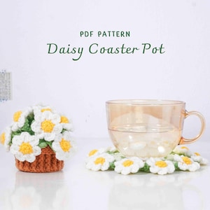 May include: A crocheted daisy coaster pot with a matching coaster and a glass mug. The coaster pot is brown with white and yellow daisy flowers. The text "PDF PATTERN Daisy Coaster Pot" is at the top.