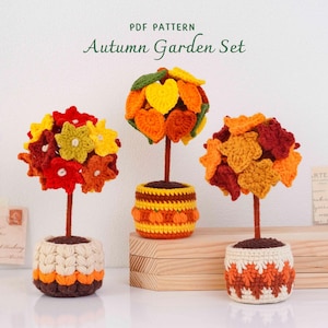 May include: Three crocheted topiary trees with autumn-coloured leaves and flowers in textured pots. The text "PDF PATTERN Autumn Garden Set" is visible at the top. The trees feature red, orange, yellow, and green yarn elements on brown stems.