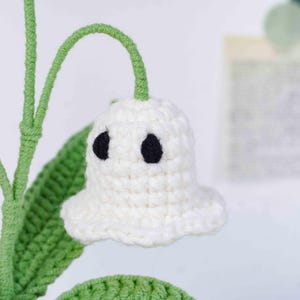 May include: A handmade crochet flower with a white bell-shaped bloom and two black eye-like details. The flower has a green stem and leaf, suggesting a craft project or decorative item.