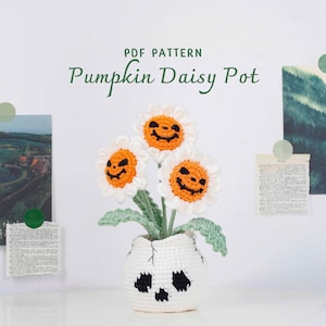Peut inclure: Un pot de marguerites citrouilles crocheté avec trois fleurs blanches et oranges, chacune avec un visage de lanterne. Le pot blanc présente des motifs de crâne noirs. Le texte "PDF PATTERN Pumpkin Daisy Pot" est visible.