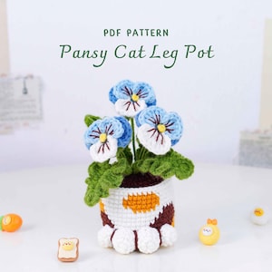 May include: A crocheted pot with blue pansies, green leaves, and a cat paw design. The pot has a white, brown, and orange pattern. The text "PDF PATTERN Pansy Cat Leg Pot" is at the top.