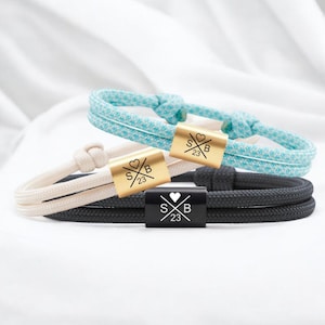 Puede incluir: Tres pulseras de amistad con nudos ajustables. Las pulseras están hechas de cuerda negra, blanca y azul. Cada pulsera tiene un dije dorado o negro con el texto "S&B 23" y un símbolo de corazón.