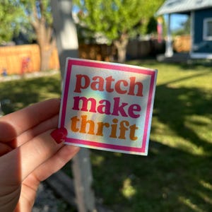 Może przedstawiać: Kwadratowa naklejka z napisem "patch make thrift" w stylu retro. Tekst jest w odcieniach różu, pomarańczy i żółci, obrysowany na biało i umieszczony na holograficznym tle. Naklejka ma różową obwódkę.