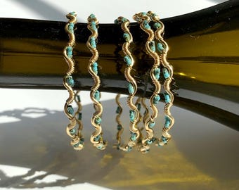 May include: Gold-toned wire bracelets with turquoise beads. The bracelets have a wavy design, with the turquoise beads evenly spaced along the wire. The bracelets are displayed on a dark surface.