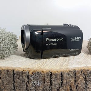 May include: A black Panasonic HDC-TM80 camcorder featuring Full HD 1920x1080 resolution, 3.0 mega pixels, and AVCHD built-in memory 16GB text printed on the side. The device has a silver lens ring and a compact, horizontal body design.