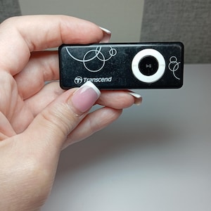 May include: A black Transcend MP3 player with a white circular control button and white decorative swirls. The player has the brand name "Transcend" printed on it.