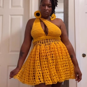 May include: A yellow crochet dress with a halter neckline and a sun-shaped design on the straps. The dress has a fitted bodice and a flowing skirt.