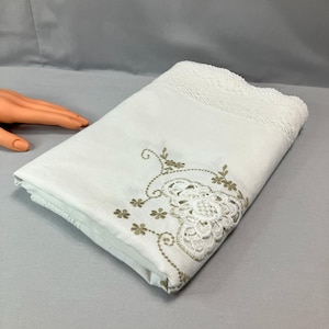 May include: White tablecloth with a delicate lace trim and embroidered floral design in gold thread.