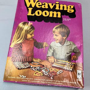 May include: A vintage box for a weaving loom toy. The box features a colorful illustration of two children using the loom. The text on the box reads "Weaving Loom" and "For Ages 4 to 14".