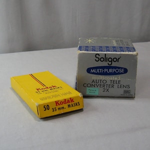 May include: Two boxes of camera accessories. A yellow box labeled "Kodak 35 mm. MASKS 50" and a silver box labeled "Soligor MULTI-PURPOSE multicoated AUTO TELE CONVERTER LENS 2X".