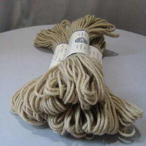 May include: Two skeins of beige yarn, wrapped in white paper with blue text that reads "The Alpaca Yarn Co. Ltd.  Made in Peru."