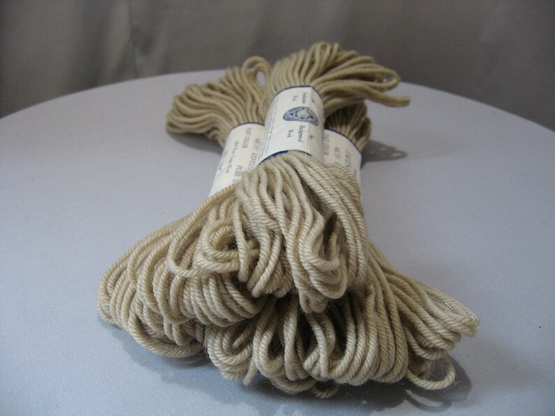 May include: Two skeins of beige yarn, wrapped in white paper with blue text that reads "The Alpaca Yarn Co. Ltd.  Made in Peru."