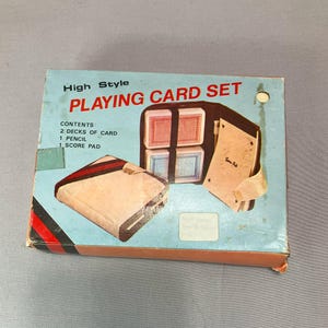 May include: Vintage "High Style Playing Card Set" in a light blue box. The set includes two decks of cards, a pencil, and a score pad, all housed in a brown case. The box has red and black stripes on the side.