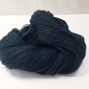 May include: A skein of dark navy blue yarn with a twisted, multi-ply construction. The fiber has a matte texture and features subtle, tiny flecks of lighter colored fibers distributed throughout the deep blue strands of the yarn.