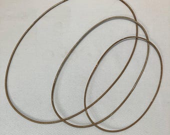 Puede incluir: Tres aros ovalados de metal oxidado de diferentes tamaños se entrelazan. El aro más grande está en la parte superior, con dos aros más pequeños superpuestos debajo. El metal tiene un aspecto envejecido, lo que sugiere uso en exteriores.