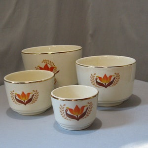 Puede incluir: Conjunto de cuatro cuencos de cerámica blanca con borde dorado y un diseño floral con tulipanes naranja y marrón. Los cuencos están anidados en orden de tamaño.