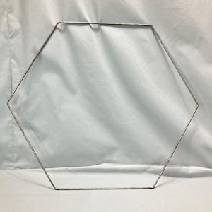 May include: A hexagonal metal frame with a slightly rusted appearance. The frame is made of thin, silver-colored wire and is displayed against a white background. The shape suggests a craft or decorative item.