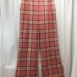 May include: Wide-leg pants with a plaid pattern in shades of coral, white, orange, and purple. The pants are hanging on a white hanger against a white background. The fabric has a textured appearance.