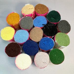May include: Assortment of 16 spools of rug yarn in various colors, including yellow, blue, green, brown, beige, and gray. The spools are arranged in a circle on a white surface.
