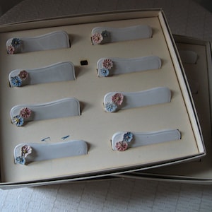 Könnte beinhalten: Eine weiße Box mit 10 Platzkarte-Haltern. Jeder Halter hat eine weiße Karte mit einem kleinen floralen Design in Rosa, Blau und Weiß.