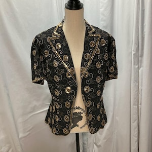 May include: Black short-sleeved jacket with gold sequin and embroidered detailing. The jacket has a notched collar and is decorated with circular and swirling patterns. The garment is displayed on a mannequin against a white backdrop.