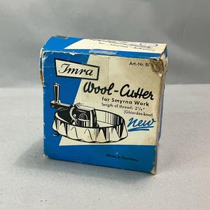 May include: A blue and white box with the text "Imra Wool-Cutter for Smyrna Work length of thread: 2 1/4" (Ghiordes-knot) new" and "Made in Germany". The box contains a metal wool cutter.