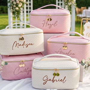 Puede incluir: Una colección de neceseres rectangulares en tonos rosa suave y crema, con un patrón tejido texturizado, cremalleras doradas con doble tirador circular y nombres bordados en letra cursiva marrón en la parte frontal de cada bolsa.